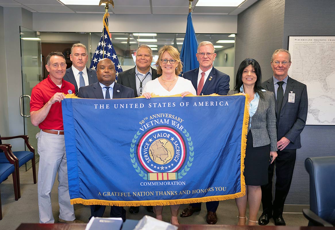 FEMA Administrator, Deputy Administrator, Roxana Allen, and other staff smiling and holding a flag